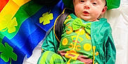 Walker is registered to the contest to win money with this photo: baby, infant, leprechaun_costume, green_hat, pot_of_gold, gold_coins, rainbow_background, shamrock, clover_pattern, bow_tie, green_clothing, striped_pants, portrait, celebration, holiday_photo, cute, barefoot, fabric, bright_colors, lying_down