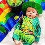 Walker is registered to the contest to win money with this photo: baby, infant, leprechaun_costume, green_hat, pot_of_gold, gold_coins, rainbow_background, shamrock, clover_pattern, bow_tie, green_clothing, striped_pants, portrait, celebration, holiday_photo, cute, barefoot, fabric, bright_colors, lying_down