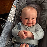 Walker joined the competition — help win amazing prizes! baby, smiling, clapping, baby_seat, gray, indoor, hand, cute, child, infant, happy, clothing, seatbelt, pacifier, wooden_floor, couch, person, portrait, playful, cozy