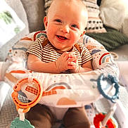 Walker is registered to the contest to win money with this photo: activity_chair, baby, child, clothing, colorful, cushion, cute, face, hand, happy, home, indoor, infant, person, play, portrait, seat, smiling, soft_toys, toy