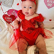 Mila joined the competition — help win amazing prizes! baby, infant, heart, valentine_decorations, red_dress, sequin, headband, bow, tongue_out, smiling, blanket, lying_down, cute, portrait, soft_texture, white_background, plush_hearts, love_you_sign, chubby_legs, holiday_photo