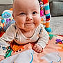 baby, infant, tummy_time, smile, chubby_cheeks, play_mat, colorful, toy, activity_gym, eyes, face, hand, onesie, indoors, soft_toys, cushion, floor, happy, portrait, close_up