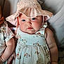 baby, infant, child, blue_eyes, sun_hat, pink_hat, dress, patterned_dress, floral_print, portrait, close_up, chubby_cheeks, cute, indoor, bed, blanket, sibling, hand, skin, smile