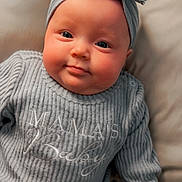 Mila is registered to the contest to win money with this photo: baby, infant, child, headband, bow, sweater, knitwear, portrait, closeup, cheeks, smile, lying_down, pillow, bed, cozy, eyes, skin, hand, clothing, blanket