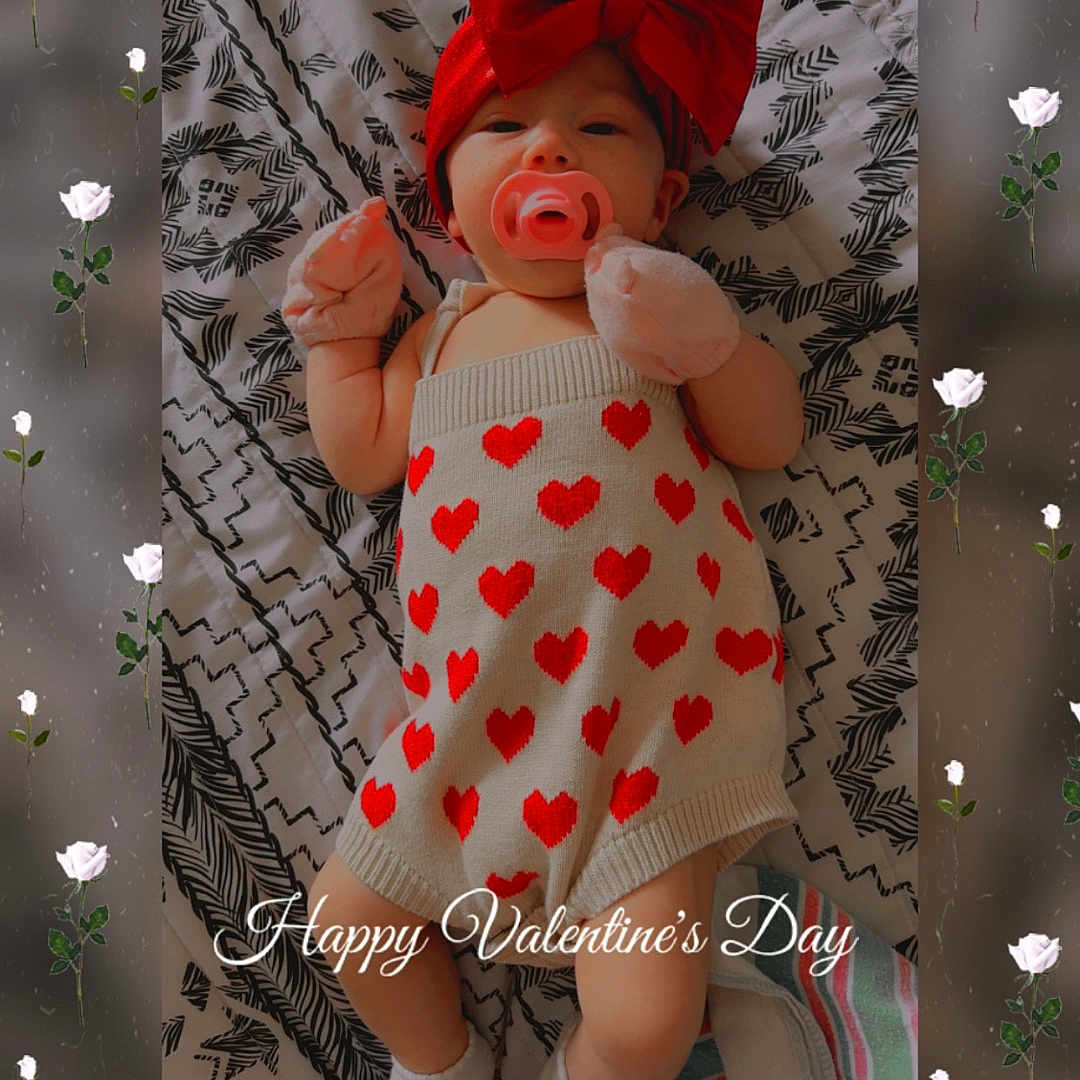 Nezuko is registered to the contest to win money with this photo: baby, infant, pacifier, red_bow, heart_pattern, blanket, patterned_blanket, gloves, socks, valentines_day, text_overlay, floral_overlay, cute, lying_down, indoors, portrait, child, headband, pink, white_roses