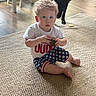 Grayson is registered to the contest to win money with this photo: child, toddler, curly_hair, white_tshirt, star_shorts, carpet, dog, black_dog, wooden_floor, indoor, furniture, table, chair, toy, person, sitting, curious, blue_eyes, home, floor