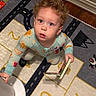 toddler, child, curly_hair, blue_eyes, pajamas, book, play_mat, numbers, roads, indoor, carpet, floor, wood_floor, furniture, home, person, cute, curious, young_child, reading