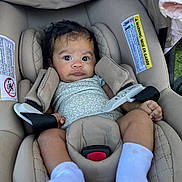 Lainie is registered to the contest to win money with this photo: baby, infant, car_seat, child, safety_belt, onesie, socks, curly_hair, wide_eyes, indoor, seat_belt, cushion, warning_label, fabric, cute, portrait, person, small_child, soft_lighting, toddler