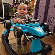 Livio participe au concours pour gagner de l'argent avec cette photo : child, toddler, baby, walker, toy_car, blue_toy, smile, smiling, christmas_tree, ornaments, holiday_decor, indoor, living_room, tile_floor, furniture, portrait, hands, eyes, cute, playtime