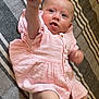 baby, infant, pink_dress, striped_blanket, lying_down, tongue_out, reaching_hand, cute, child, person, soft_fabric, playful, indoors, smiling, young, skin, face, legs, buttoned_dress, expression