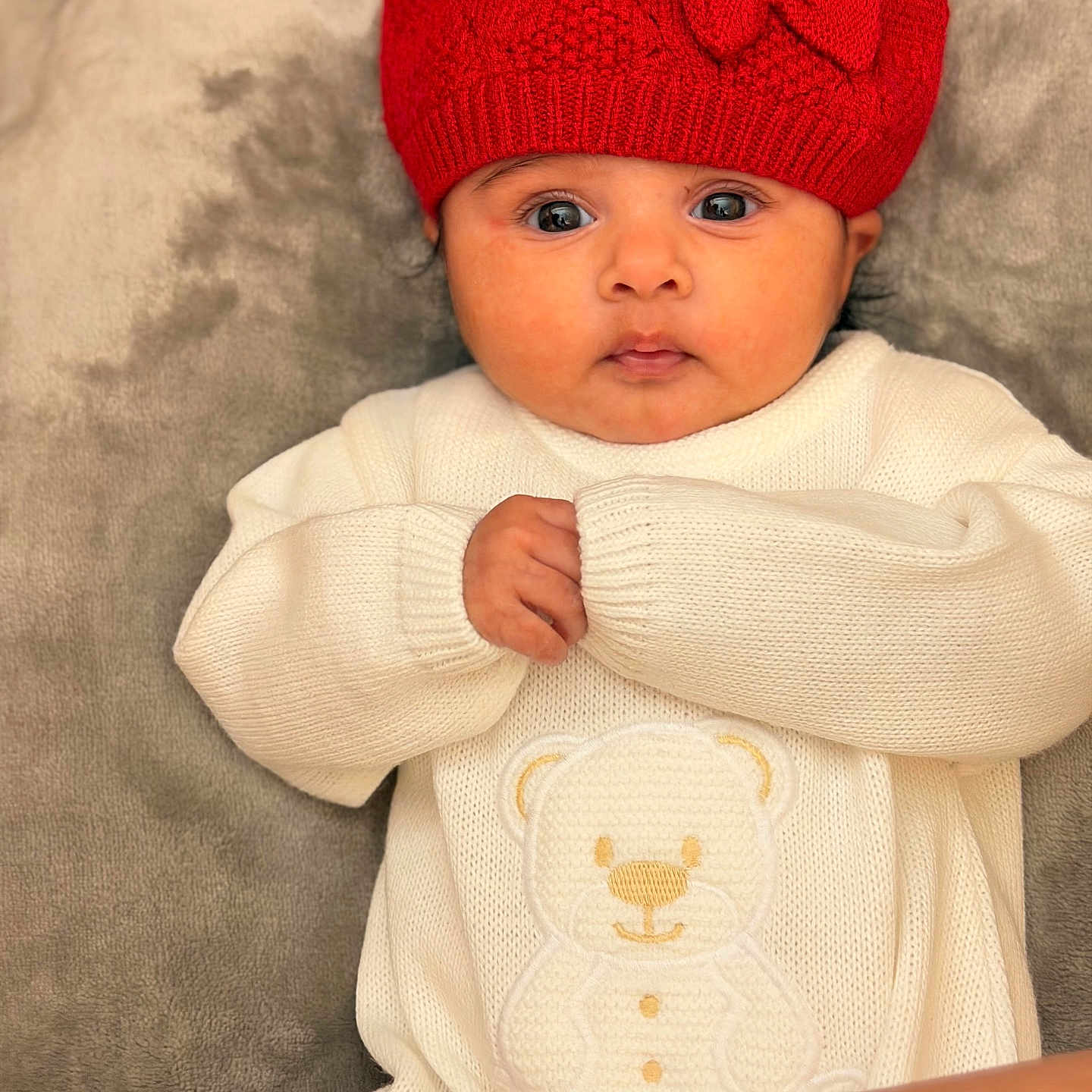 Divya is registered to the contest to win money with this photo: adorable, baby, big_eyes, blanket, child, cozy_clothing, cute, headwear, indoors, infant, knit_hat, laying_down, portrait, red_hat, soft_texture, teddy_bear_design, warm_clothes, white_sweater, winter_wear, young