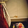 cat, window, blinds, red_cup, remote_control, glasses, table, curtains, doily, orange_liquid, indoor, pet, fluffy, peek, dim_light, blurry, fabric, home, furniture, animal