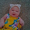 baby, infant, child, smiling, portrait, indoor, carpet, floral_dress, yellow_clothing, hair_bow, headband, lying_down, happy, face, arms, hands, colorful, text_overlay, floor, photography