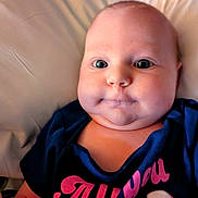 Aurora Jean joined the competition — help win amazing prizes! baby, child, face, cheeks, eyes, clothing, shirt, text_on_clothing, skin, infant, portrait, closeup, person, head, cute, expression, lying_down, indoors, soft_background, young