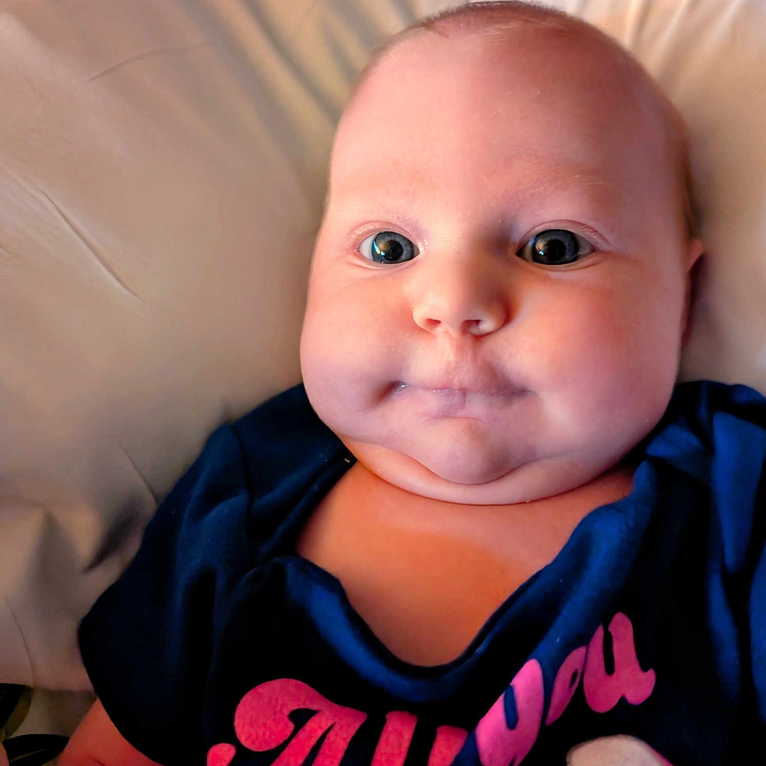 Aurora Jean joined the competition — help win amazing prizes! baby, cheeks, child, closeup, clothing, cute, expression, eyes, face, head, indoors, infant, lying_down, person, portrait, shirt, skin, soft_background, text_on_clothing, young