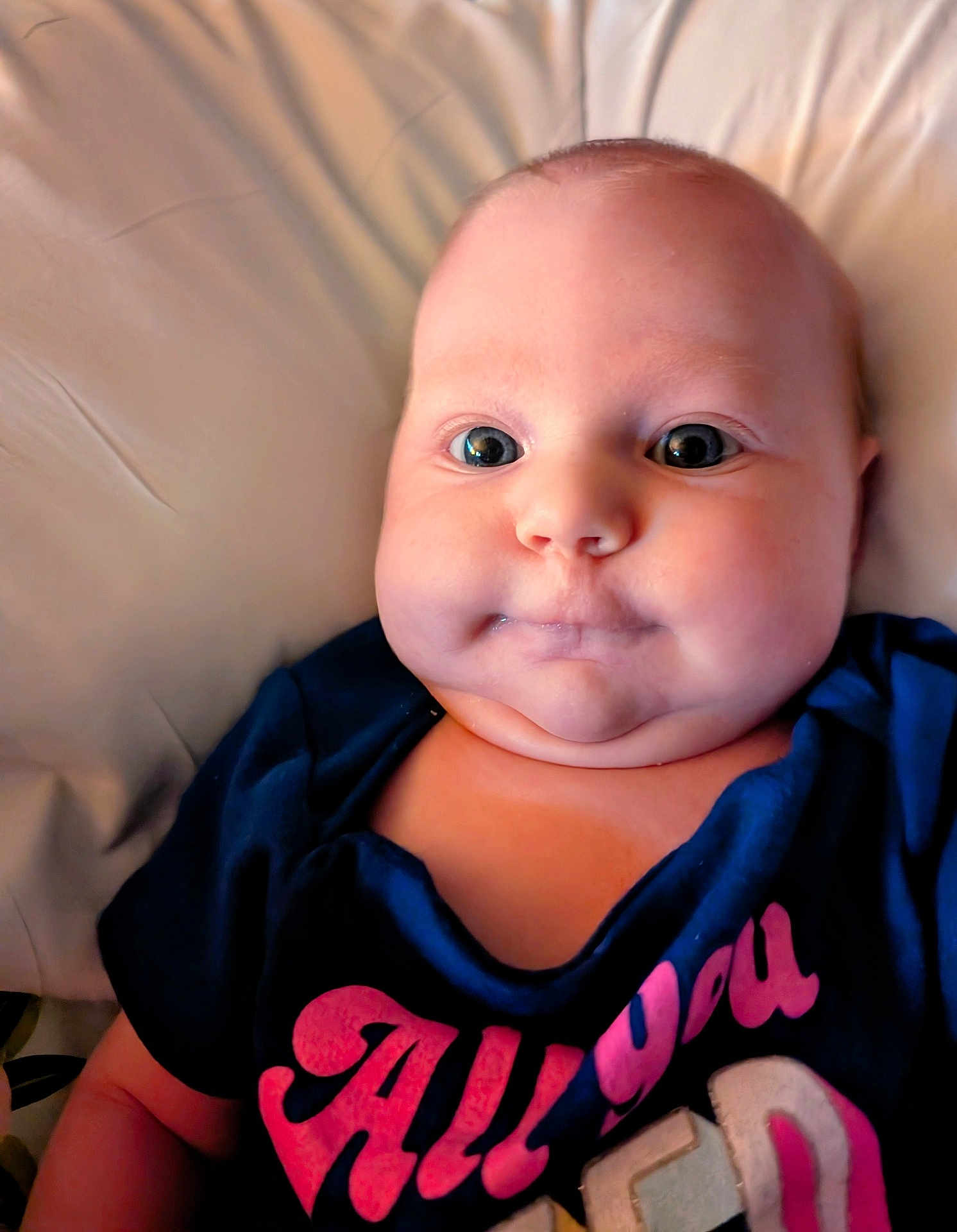 Aurora Jean joined the competition — help win amazing prizes! baby, child, face, cheeks, eyes, clothing, shirt, text_on_clothing, skin, infant, portrait, closeup, person, head, cute, expression, lying_down, indoors, soft_background, young