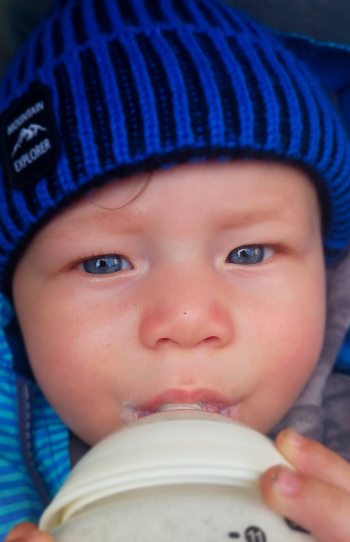 Harlem is registered to the contest to win money with this photo: baby, baby_bottle, blue, cap, cheek, chin, drinkware, eyebrow, eyelash, face, facial_expression, headwear, lip, nose, organ, person, photograph, plastic_bottle, product, skin