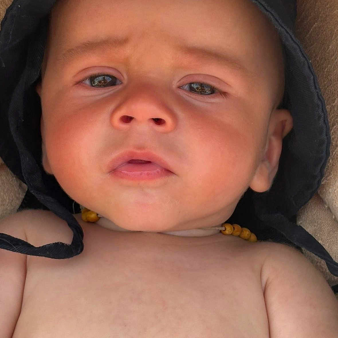 Elyias participe au concours pour gagner de l'argent avec cette photo : baby, black_hat, child, closeup, curious, expression, face, hat, headwear, human, indoors, infant, necklace, person, portrait, pout, skin, soft_surface, wooden_beads, young