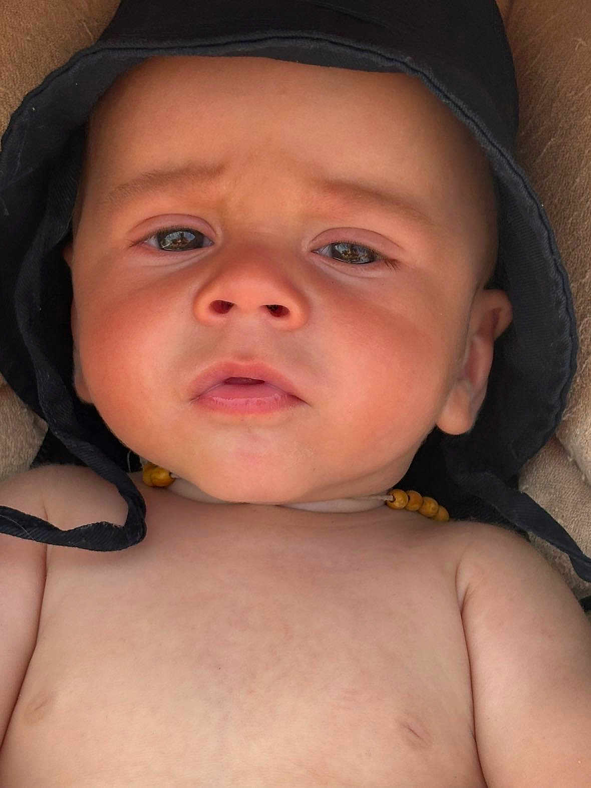 Elyias participe au concours pour gagner de l'argent avec cette photo : baby, infant, face, hat, black_hat, necklace, wooden_beads, skin, closeup, expression, curious, pout, human, child, portrait, young, headwear, indoors, soft_surface, person