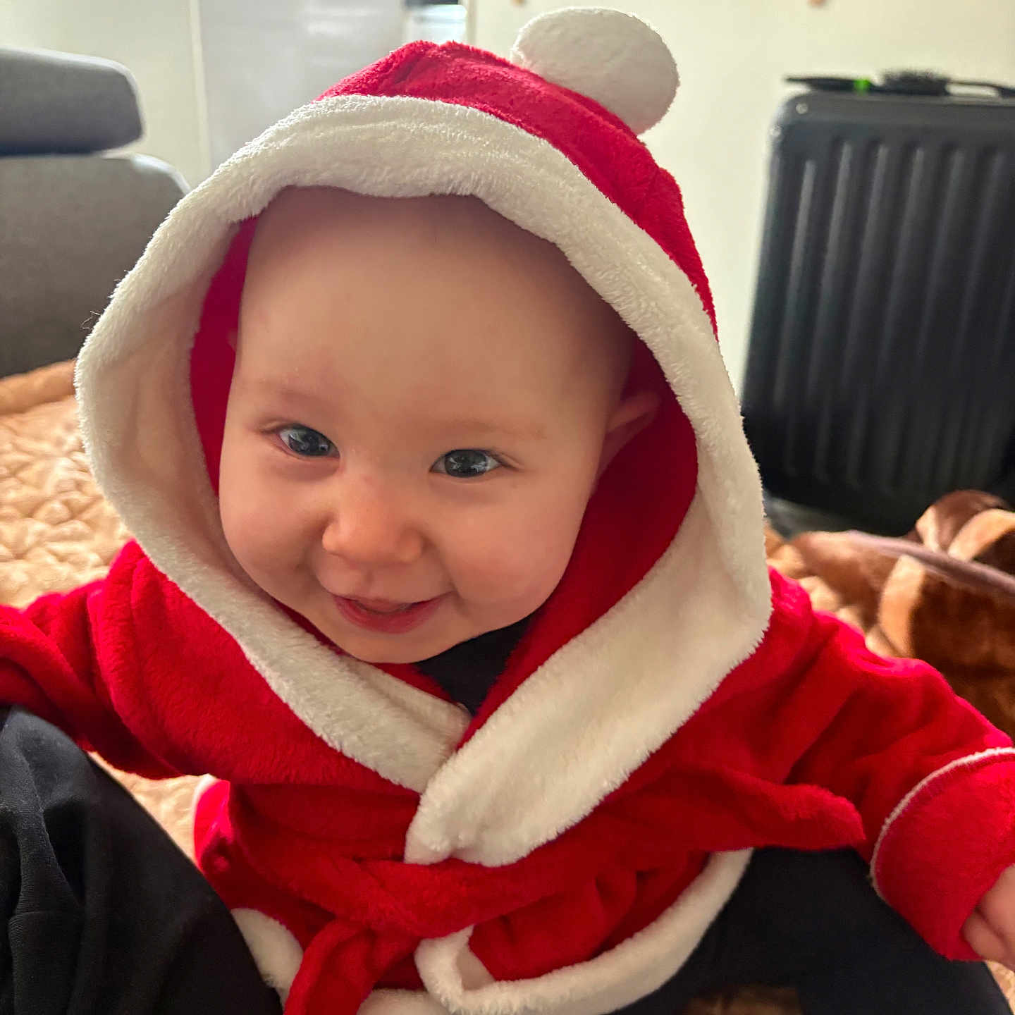 Taha a rejoint le concours — aidez-le/la à gagner de superbes lots ! apparel, baby, blanket, child, cozy, cute, face, furniture, headwear, hood, indoor, infant, joyful, person, red_clothing, room, sitting, smile, soft_texture, warm_clothing
