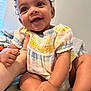 baby, child, smiling, curly_hair, pastel_clothing, indoor, person, cute, happy, infant, sitting, hand, skin, face, eyes, mouth, expression, holding, soft_light, candid