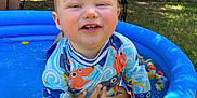 Onyx joined the competition — help win amazing prizes! backyard, blue, child, fence, grass, happy, hat, outdoor, person, play, pool, sitting, smile, sunlight, swimsuit, toddler, toy, tree, water, woman