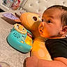Zion joined the competition — help win amazing prizes! baby, child, toy, plush, bed, pillow, face, hand, black_clothing, curious, indoor, bedroom, soft_toy, colorful, young_child, infant, closeup, person, resting, play