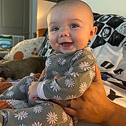 Violet is registered to the contest to win money with this photo: baby, child, smiling, onesie, floral_pattern, person, hand, indoor, happy, dog, blanket, seated, cozy, portrait, cute, face, skin, comfort, home, family