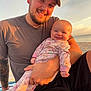 baby, beach, cap, casual_clothing, facial_hair, family, happy, holding, man, nature, ocean, outdoor, pajamas, portrait, sand, sky, smile, sunset, tattoo, warm_light