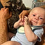baby, cat, adult_hands, smile, indoor, cozy, onesie, gray_cat, curious_cat, happy_baby, infant, close_up, portrait, human, pet, domestic_animal, holding, gentle, cute, family_moment