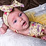 baby, infant, blue_eyes, headband, bow, yellow_outfit, cartoon_print, tutu, blanket, soft_texture, lying_down, cute, child, portrait, indoors, skin, hand, expression, clothing, person