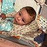baby, infant, child, portrait, face, eyes, looking_up, smiling, indoors, nursery, crib, blanket, diaper, stuffed_animal, floral, patterned, pajamas, seated, cozy, photography