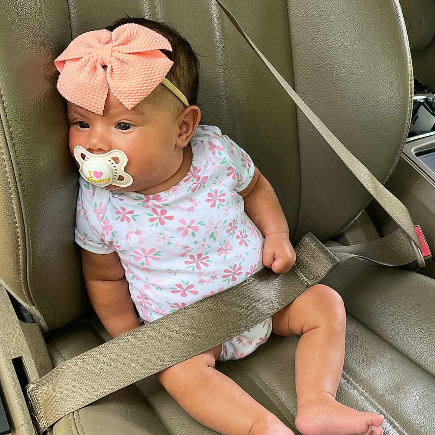 Alamae is registered to the contest to win money with this photo: baby, car_interior, car_seat, child, cute, floral_pattern, foot, hand, headband, infant, leather_seat, onesie, pacifier, pink_bow, portrait, safety, seat_belt, sitting, skin, young_child