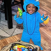 Josiah is registered to the contest to win money with this photo: toddler, child, costume, cookie_monster, blue, candy, bag, floor, wooden_floor, happy, smiling, indoor, beads, purple, toy, celebration, clothing, person, furniture_leg, footwear