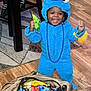 toddler, child, costume, cookie_monster, blue, candy, bag, floor, wooden_floor, happy, smiling, indoor, beads, purple, toy, celebration, clothing, person, furniture_leg, footwear