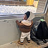 Tymir joined the competition — help win amazing prizes! toddler, child, winter_clothing, hood, boots, smile, window, snow, indoor, backpack, plastic_bag, concrete, wall, floor, face, looking, standing, person, cold_weather, casual