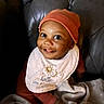 baby, smiling, hat, bib, face, child, indoor, blanket, couch, leather, portrait, cute, happy, infant, young_child, clothing, headwear, sitting, expression, cozy
