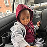 toddler, child, car_seat, hoodie, gray_sweatpants, shoe, car_interior, window, brick_building, rain, seatbelt, cup_holder, curious, casual_clothing, indoors, portrait, young_child, seat, person, looking_down