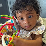 Ayla is registered to the contest to win money with this photo: baby, child, toy, colorful, curly_hair, blanket, indoor, face, hand, expression, person, infant, clothing, play, cute, portrait, young, skin, closeup, rest