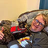 Gigi is registered to the contest to win money with this photo: animal, blanket, casual, cat, clothing, comfort, couch, eyewear, glasses, hand, human, indoor, man, pet, portrait, relaxed, resting, service_dog_vest, smiling, tortoiseshell_cat