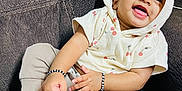 Arha is registered to the contest to win money with this photo: baby, child, smile, hoodie, cherry_print, bracelet, anklet, couch, sitting, happy, cute, clothing, person, indoors, portrait, infant, skin, hand, foot, jewelry
