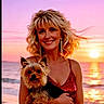animal, beach, blonde_hair, curly_hair, dog, earrings, happy, holding, ocean, outdoor, pet, portrait, red_dress, reflection, sky, smile, sunset, water, woman, yorkshire_terrier