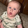 Liam is registered to the contest to win money with this photo: baby, infant, dinosaur_print, onesie, bed, wooden_headboard, surprised_expression, blue_eyes, sitting, flash_photography, indoor, child, cute, skin, face, mouth_open, short_hair, person, furniture, home