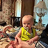 baby, infant, pacifier, yellow_clothing, tattoo, hand, bed, quilt, blanket, arm, furniture, wardrobe, lamp, vintage, curtains, room, indoor, person, holding, portrait