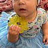 baby, child, tutu, headband, yellow_toy, flower_toy, barefoot, blue_dress, curious_expression, indoor, blanket, patterned_blanket, sitting, cute, portrait, closeup, infant, young_child, hand_holding_toy, playtime