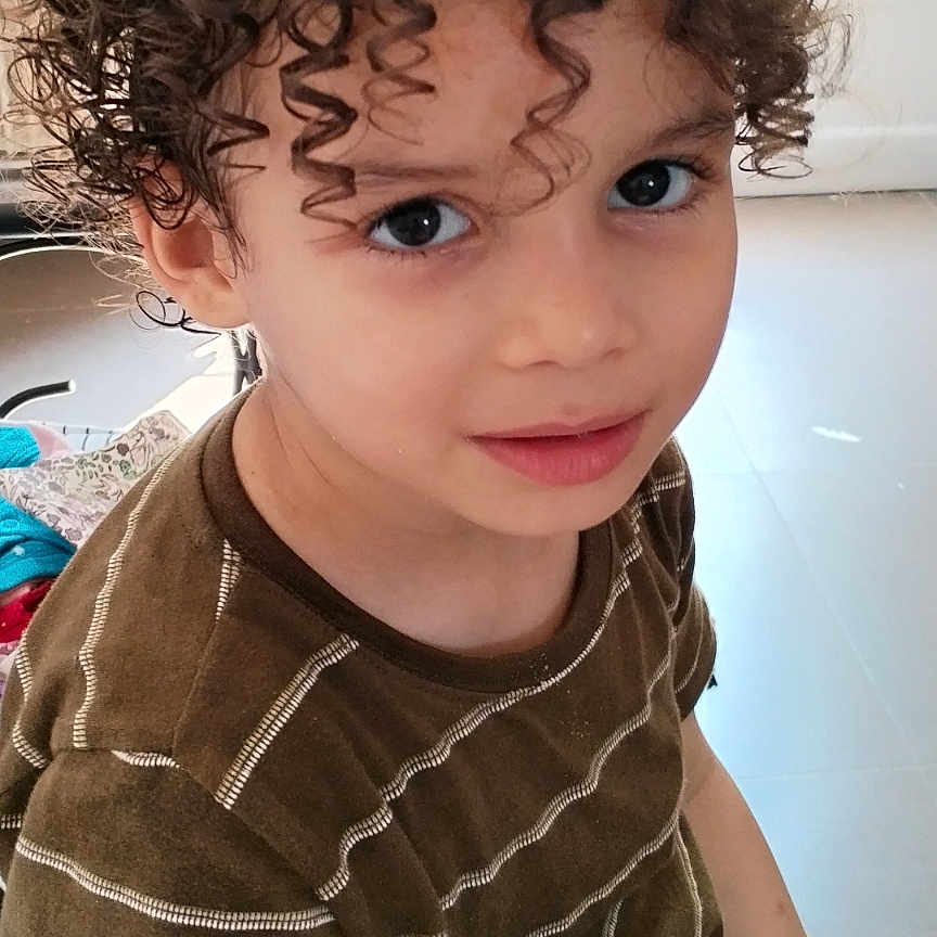 Nidal a rejoint le concours — aidez-le/la à gagner de superbes lots ! bright, brown_shirt, casual_clothing, child, childhood, curly_hair, cute, eyes, face, hair, home, indoor, looking_up, natural_light, person, portrait, seated, smiling, window, young