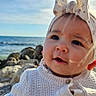 baby, child, infant, headband, bow, sweater, knitted, ocean, sea, rocks, sky, outdoor, portrait, cute, person, hand, warm_clothing, daylight, nature, smile