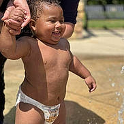Dominic joined the competition — help win amazing prizes! toddler, child, diaper, water, hand_holding, smiling, outdoor, sunlight, wet_skin, adult_hand, playful, happy, summer, fountain, closeup, person, baby, skin, fun, daytime