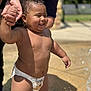 toddler, child, diaper, water, hand_holding, smiling, outdoor, sunlight, wet_skin, adult_hand, playful, happy, summer, fountain, closeup, person, baby, skin, fun, daytime