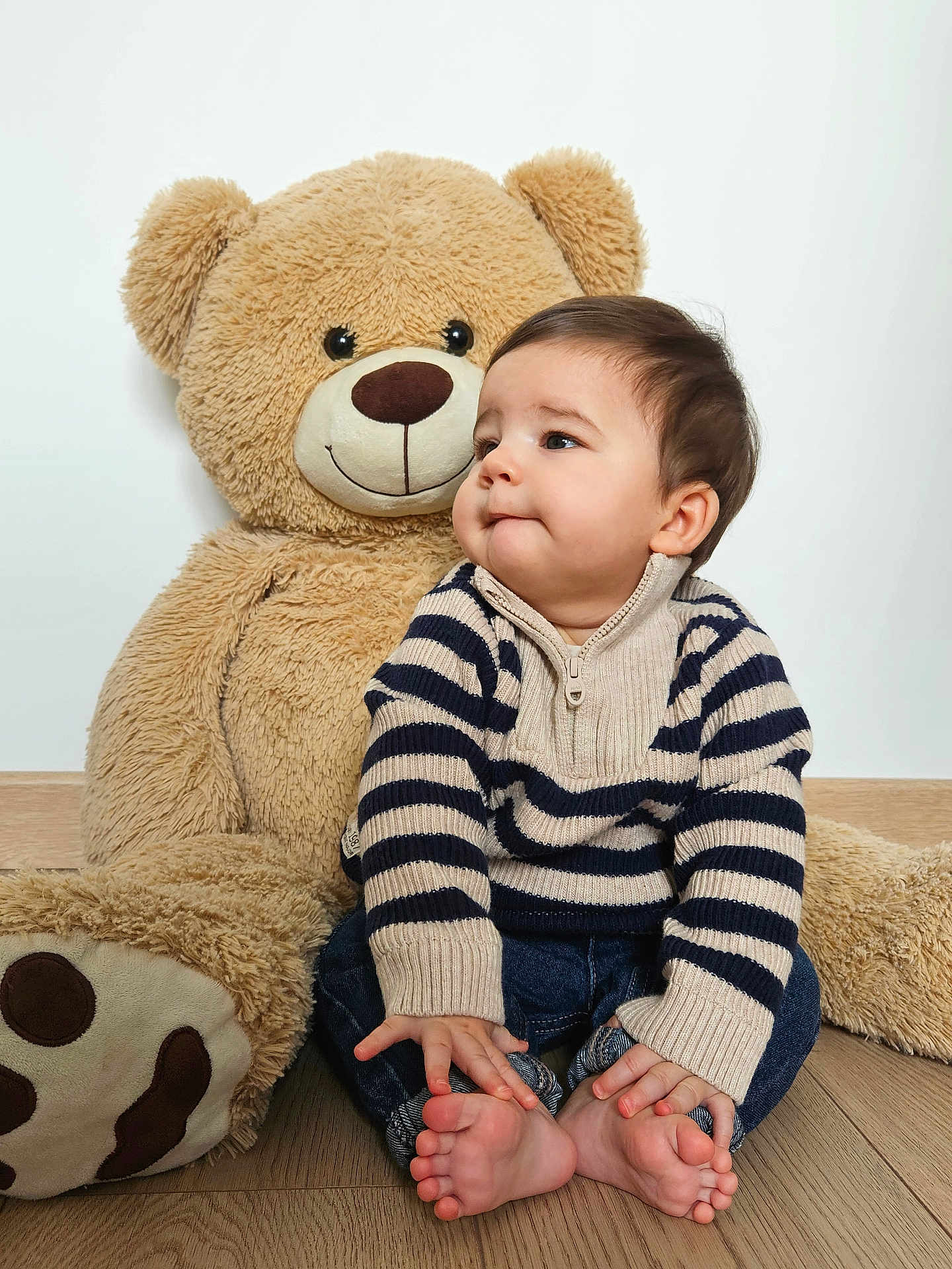 Maylone a rejoint le concours — aidez-le/la à gagner de superbes lots ! baby, toddler, teddy_bear, plush_toy, child, portrait, indoor, cute, striped_sweater, jeans, bare_feet, smile, soft_toy, wood_floor, sitting, face, fur, white_wall, cozy, playful